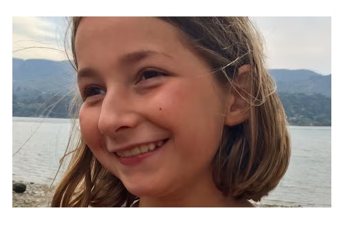 Martha smiles, her face slightly side on to the camera, in front of a lake